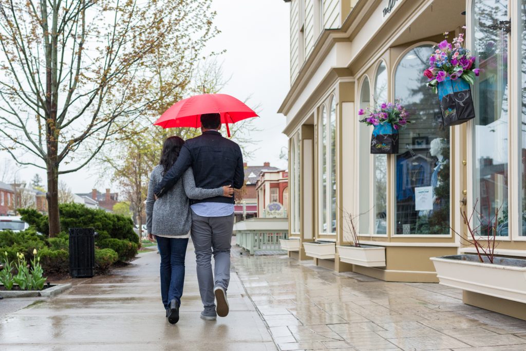 Couple with red umbrella walking down the street - Niagara on the Lake Engagement Photography
