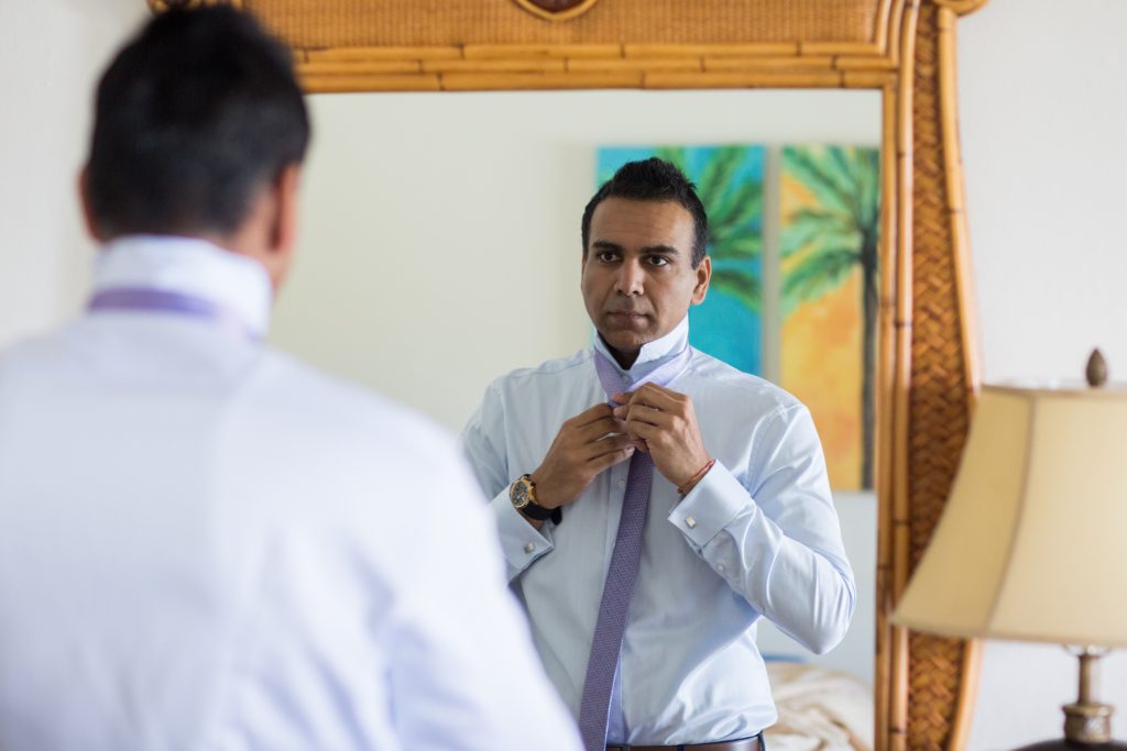 Groom getting ready tying his tie in the mirror