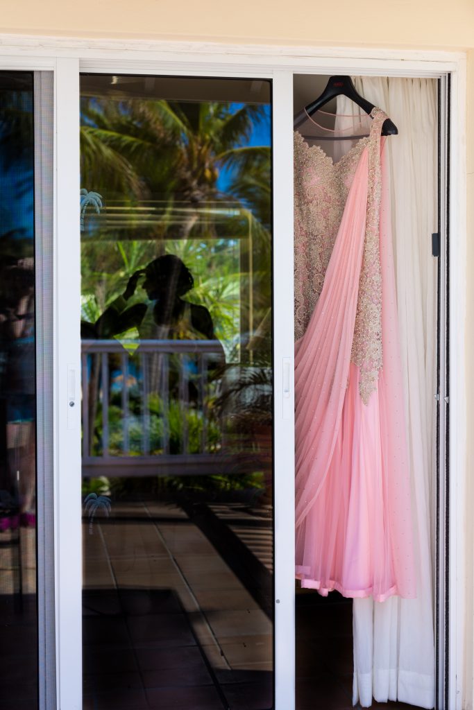Pink bridal sari hanging up while the bride gets her makeup done before her Indian destination wedding ceremony