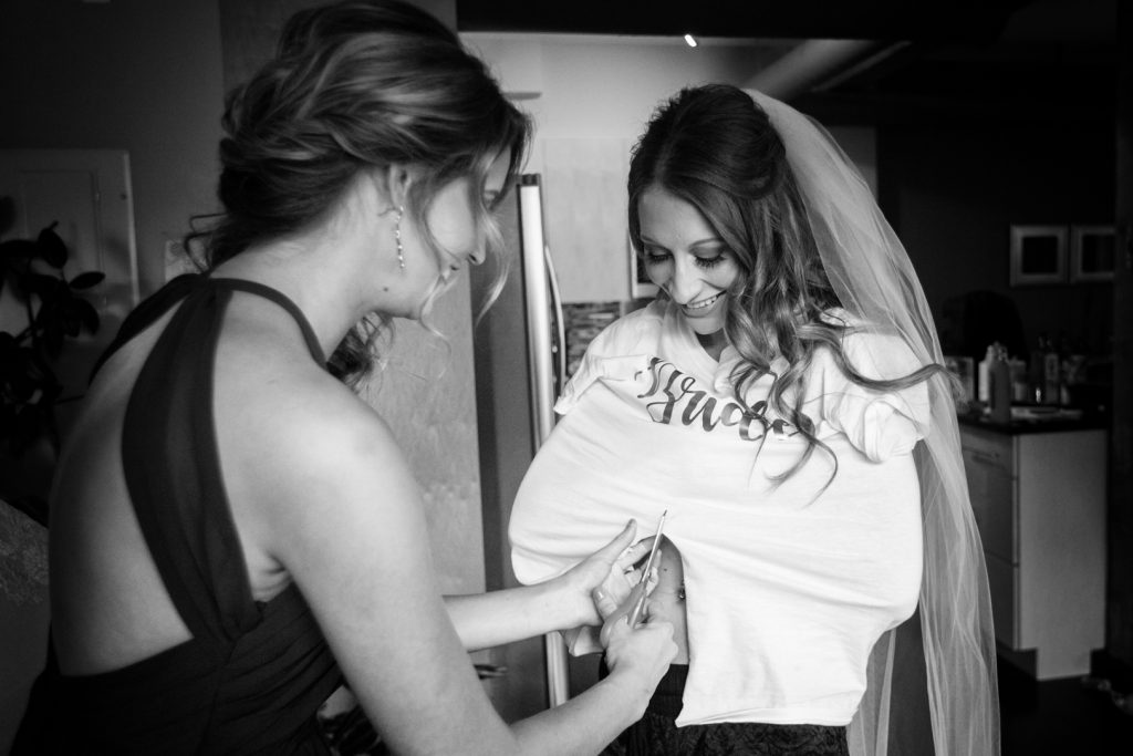 Maid of honour helps the bride cut off her t-shirt before putting on her wedding dress for Shaw Conference Centre wedding