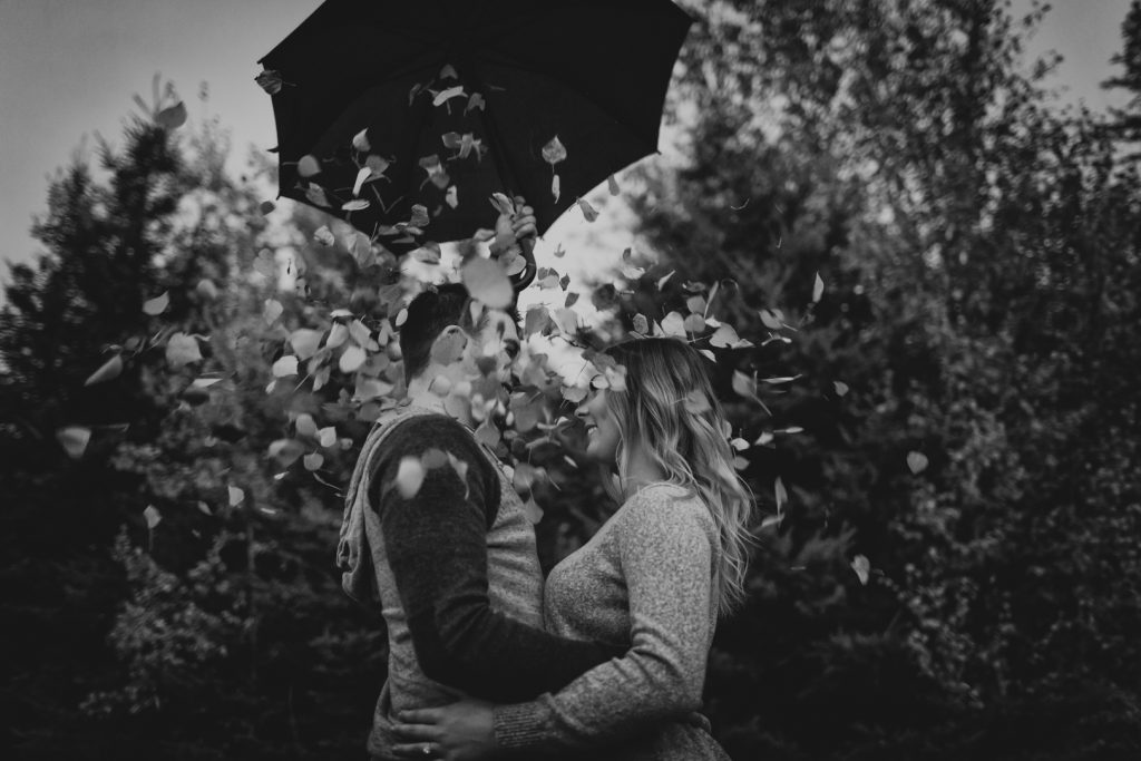 Couple stand under the falling leaves during their autumn engagement session